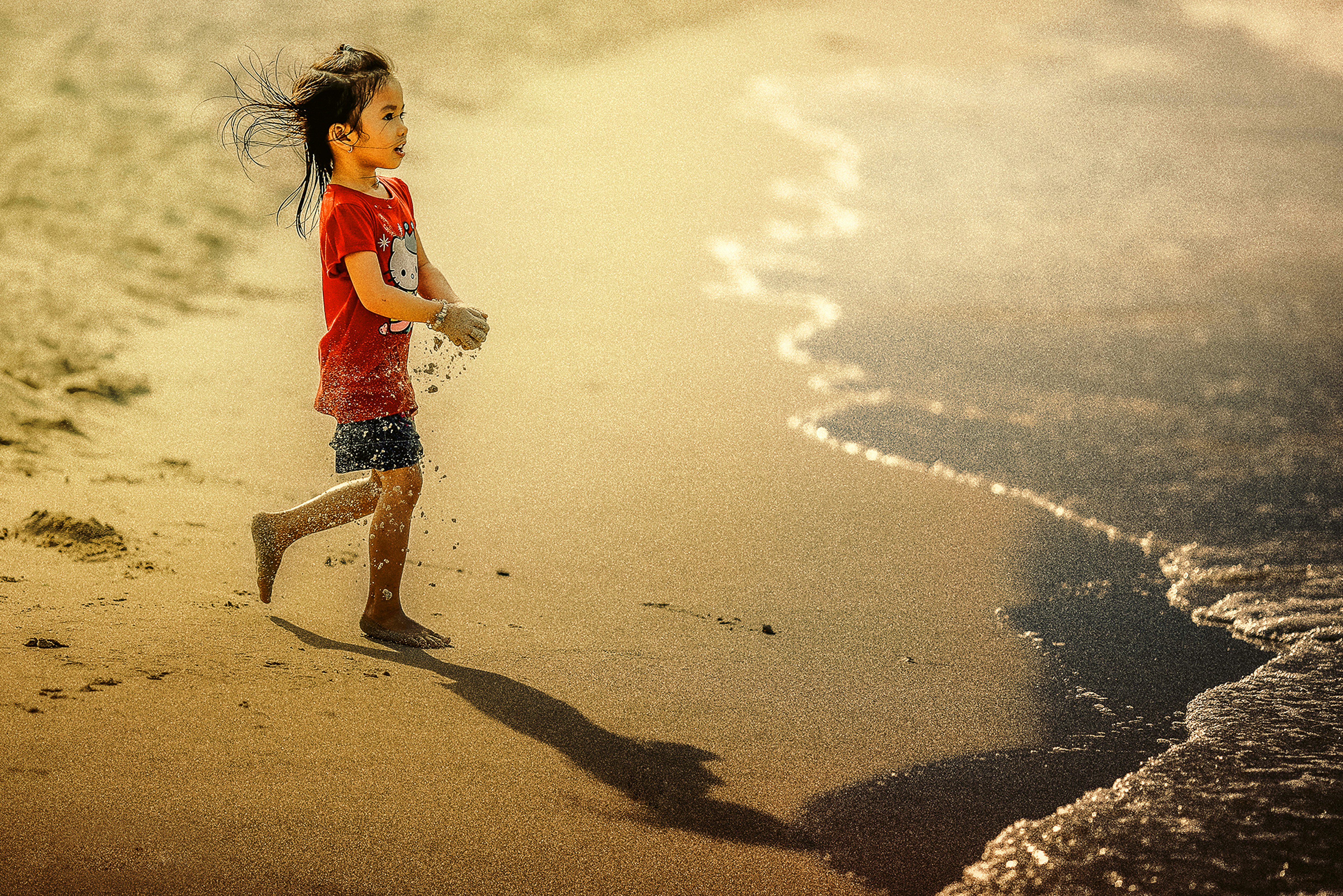 girl carrying sand on her hands while walking towards body of water